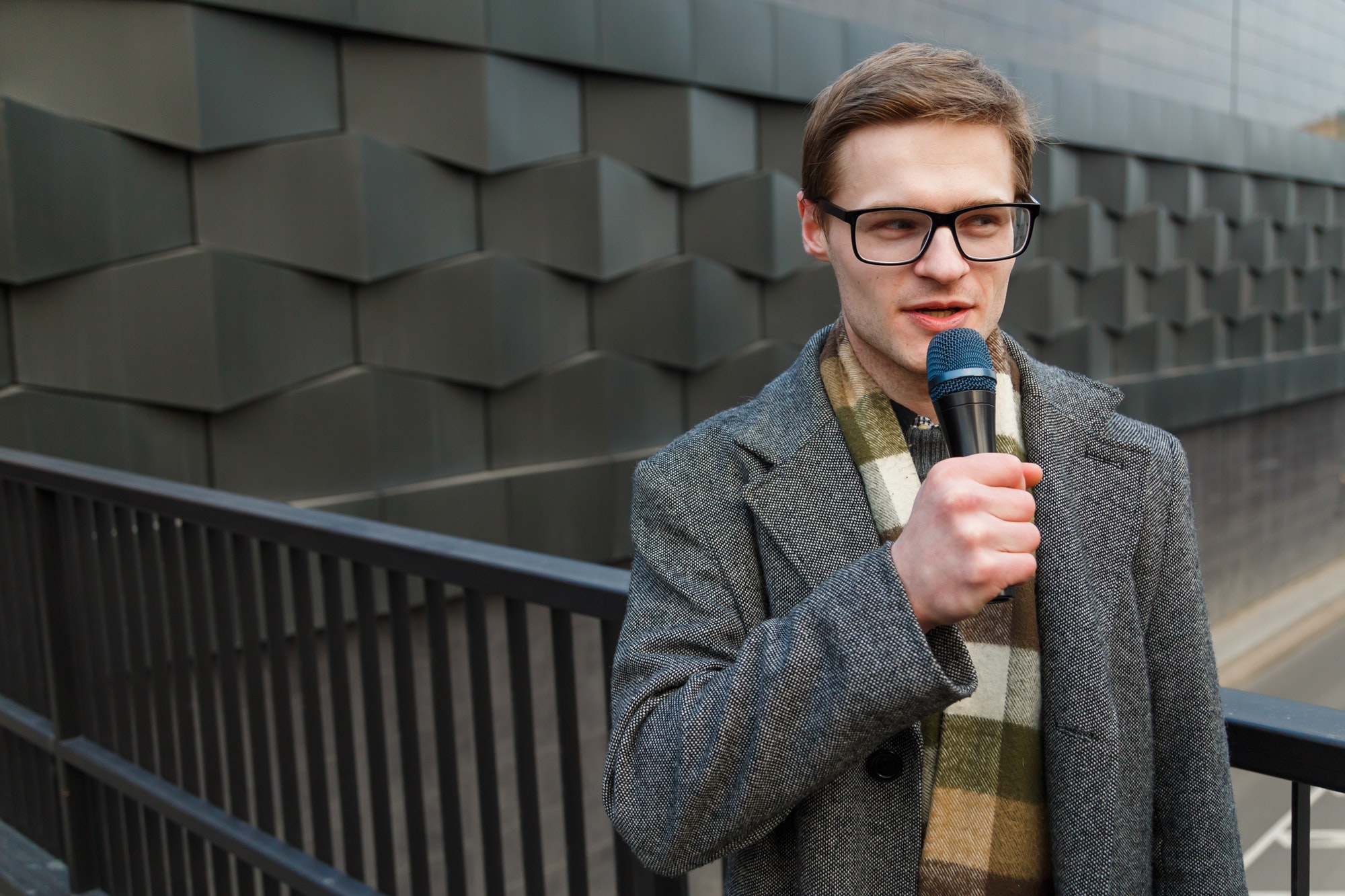 Young news reporter with microphone is broadcasting on the street. Fashion or business news.