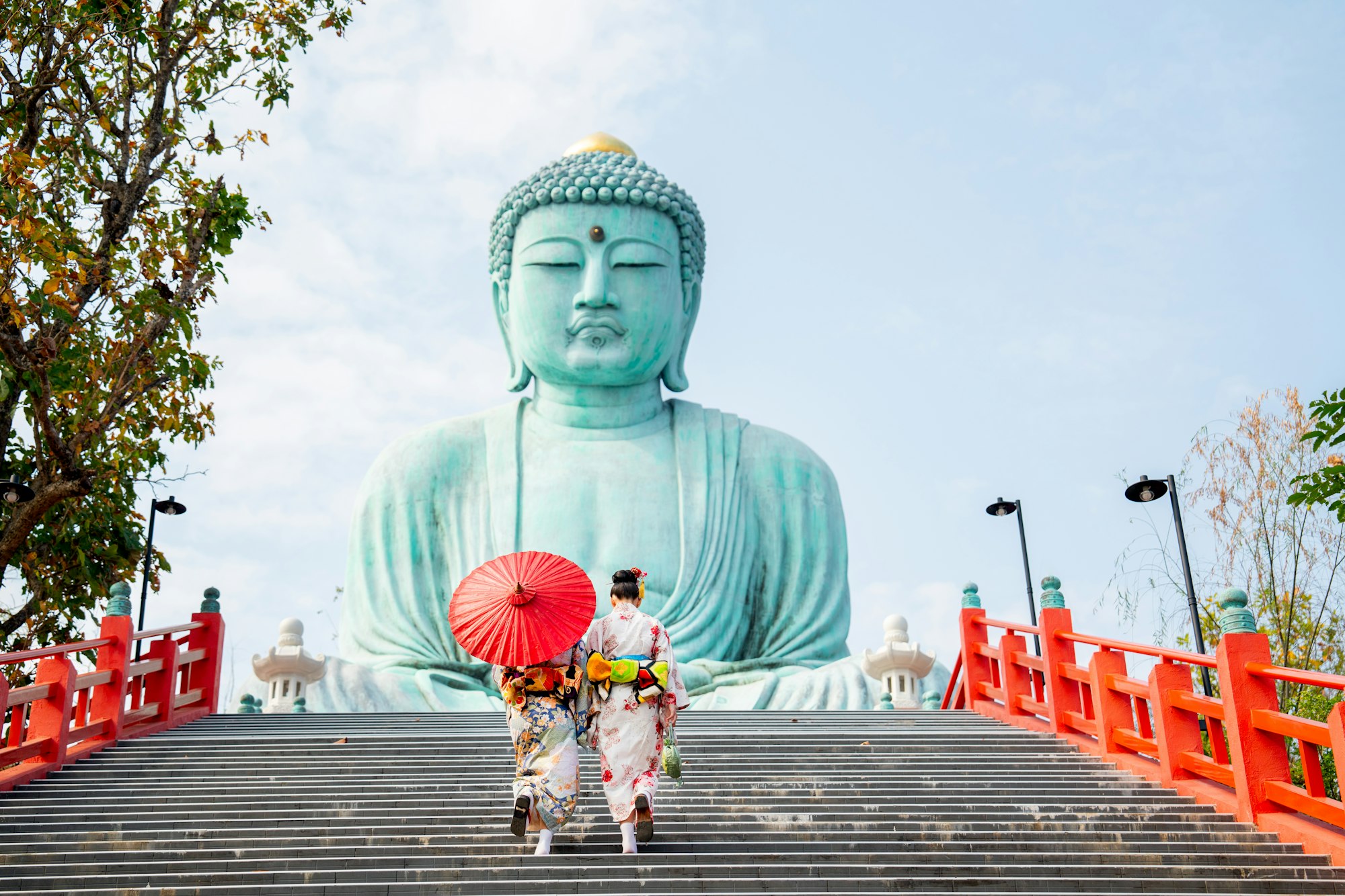 Back of two Asian young woman with japanese style dress walk up on stair to green big buddha