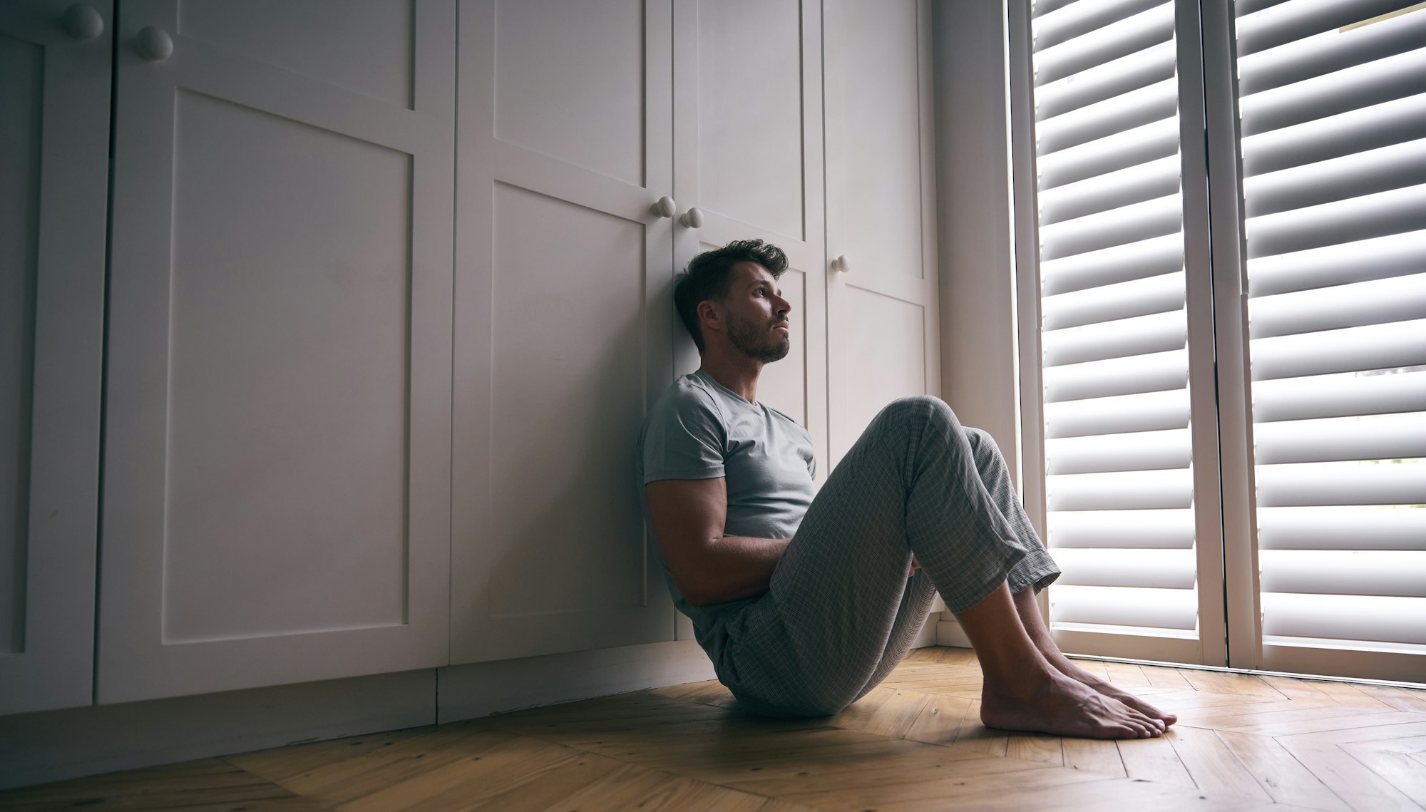 Depressed Man Suffering With Poor Mental Health Sitting On Floor At Home