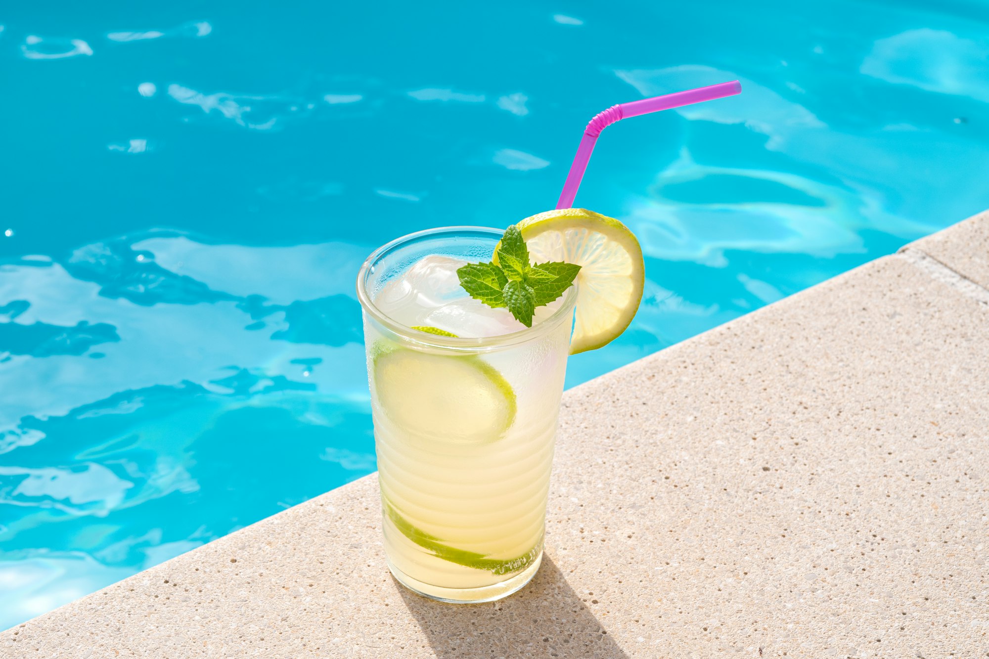 Fresh drinking glass with straw on a swimming poll border