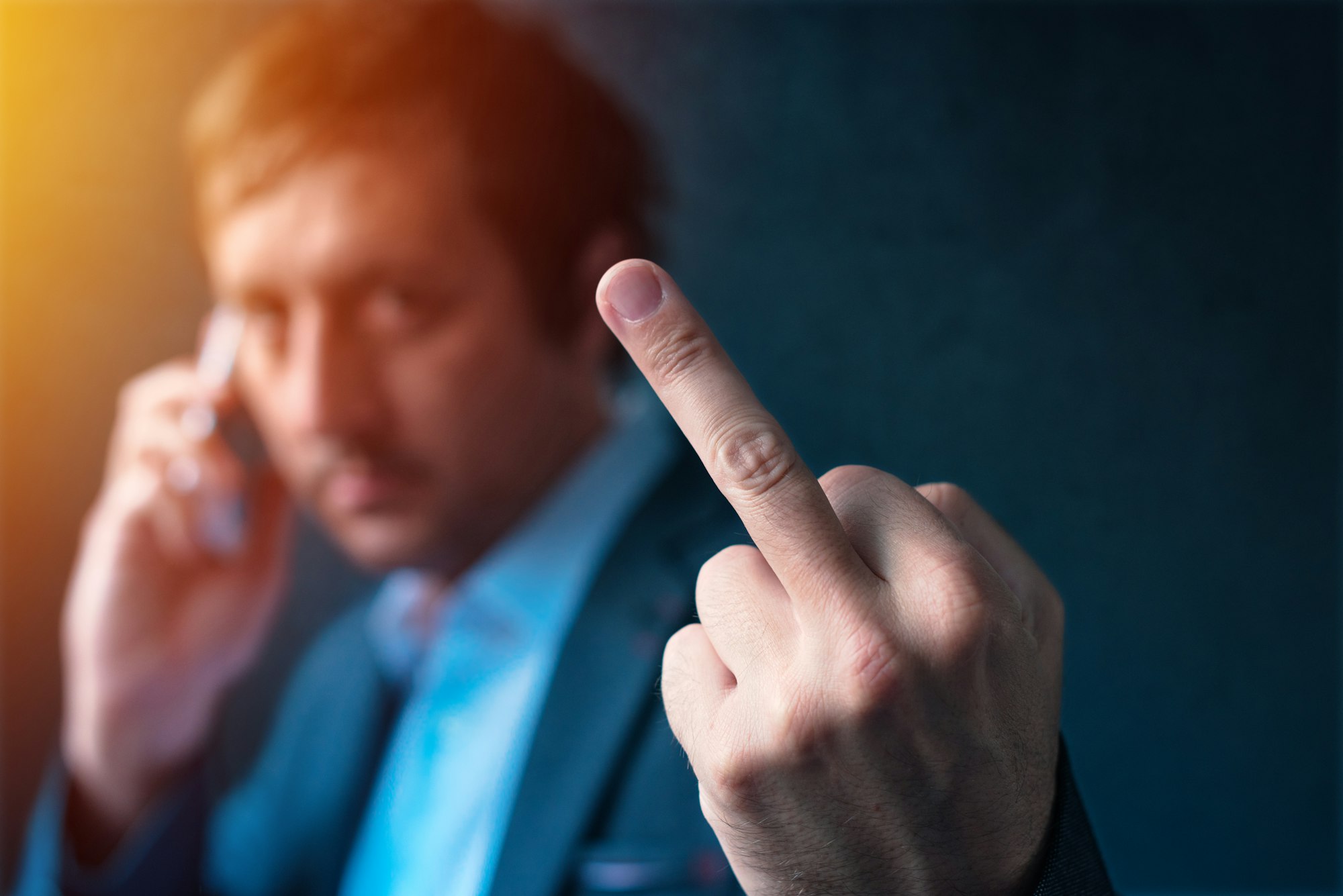 Rude businessman talking on phone and giving middle finger