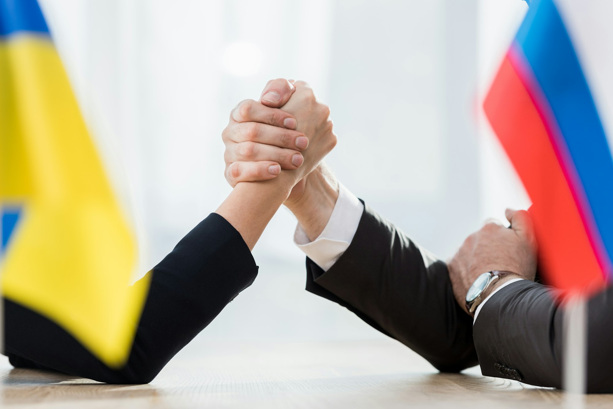 selective focus of diplomats holding hands near ukrainian and russian flags