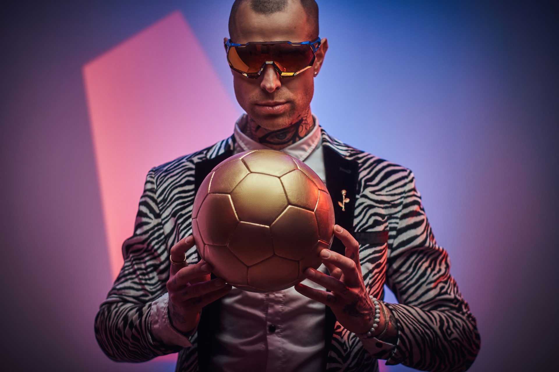 Strange styled guy poses with golden ball in abstract background