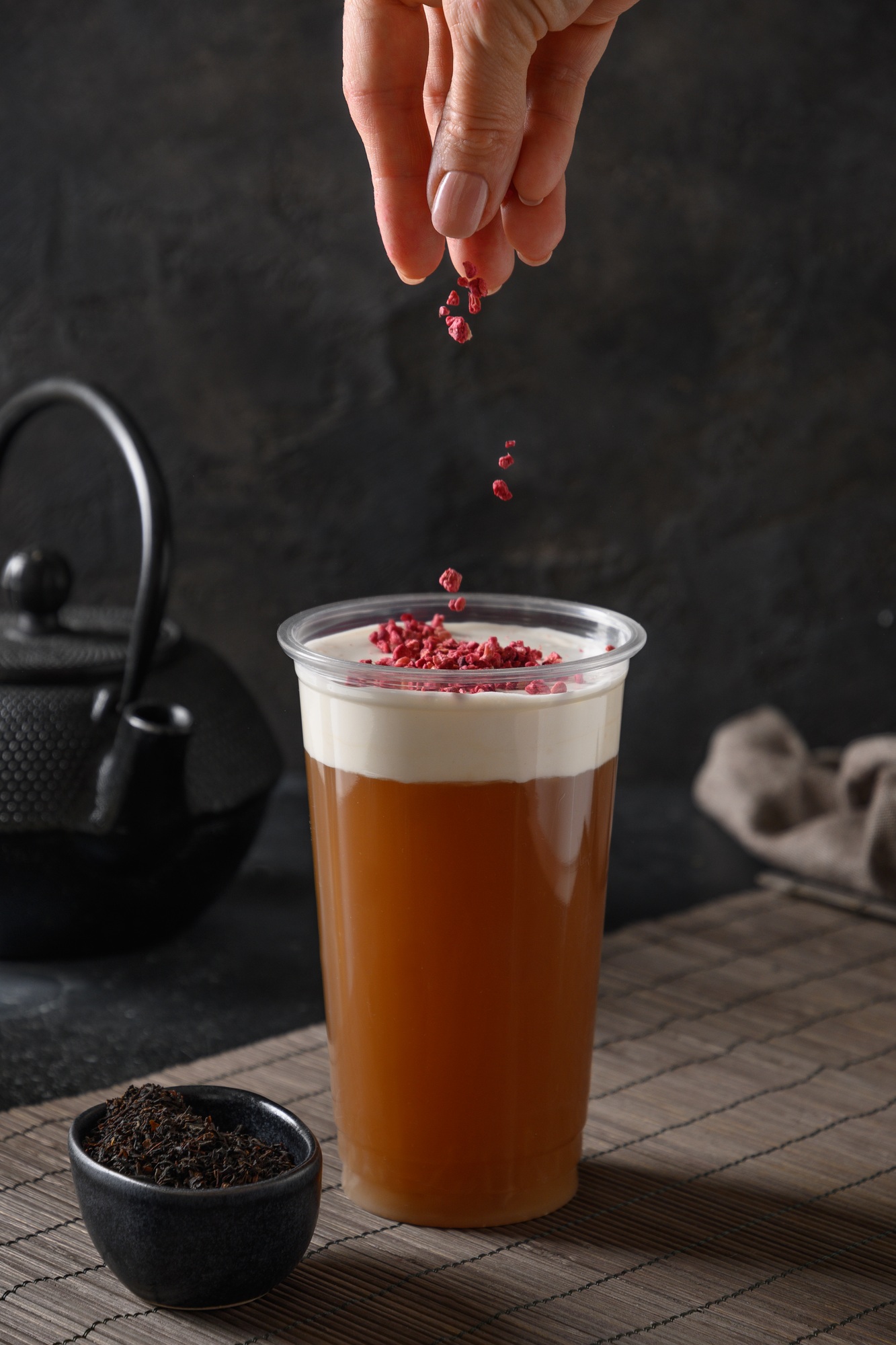 Woman sprinkles cheese tea with whipped cream topped berrires.